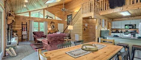 A spacious wooden cabin with a dining area, kitchen, and a loft bedroom.