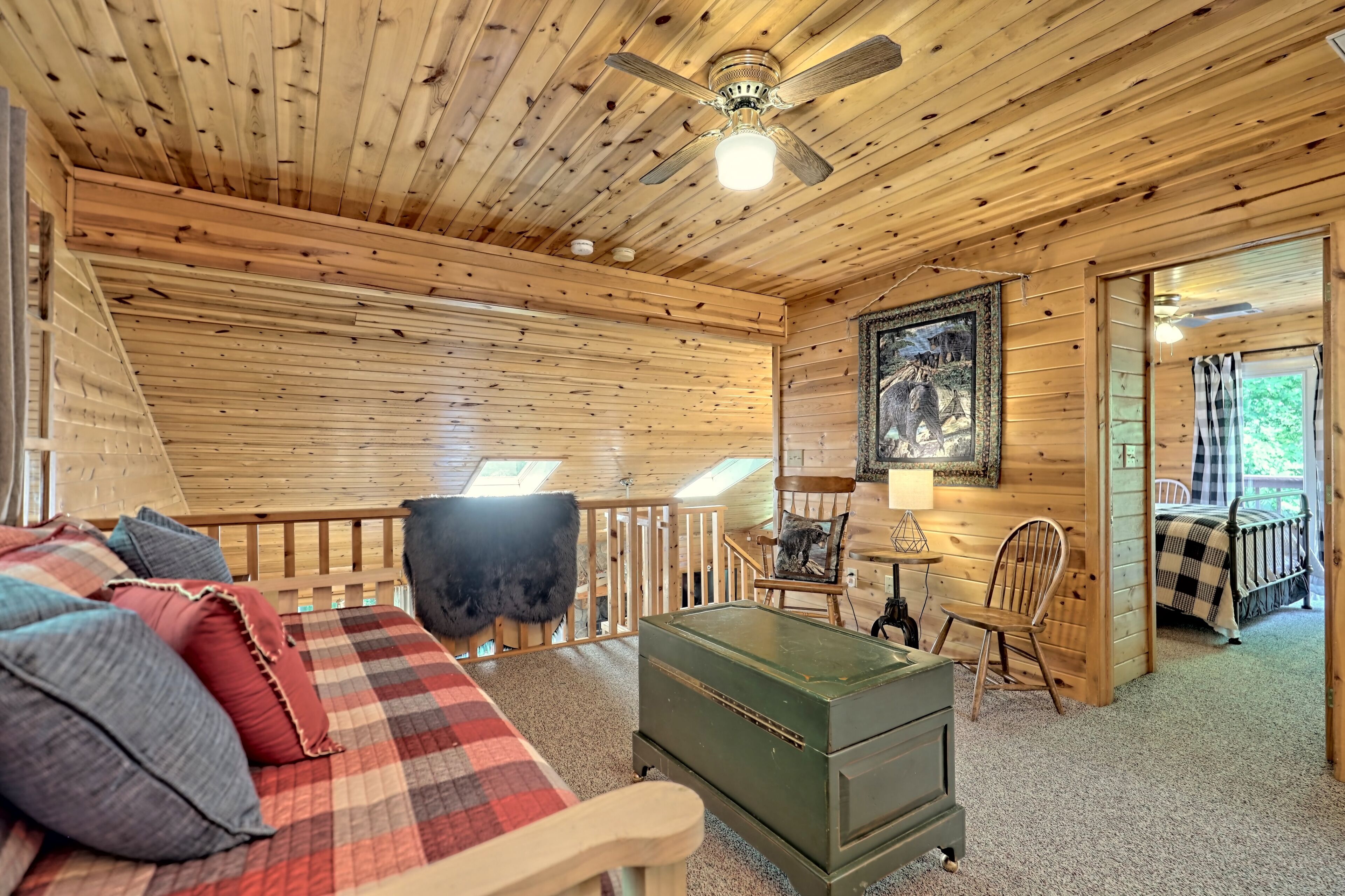 A cozy cabin interior with a wooden ceiling, a plaid bed, a green dresser, and a chair.