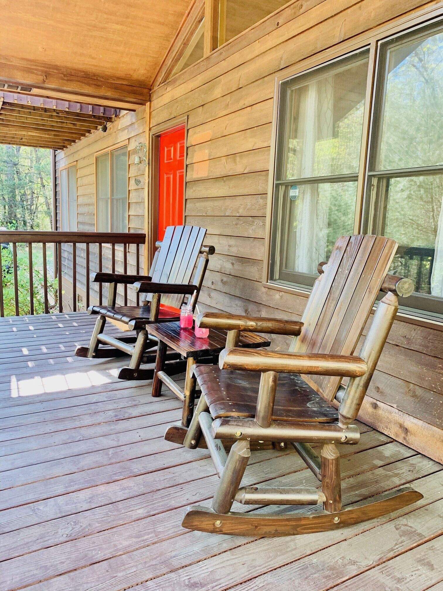 A wooden porch with rocking chairs and a table, overlooking a forested area.