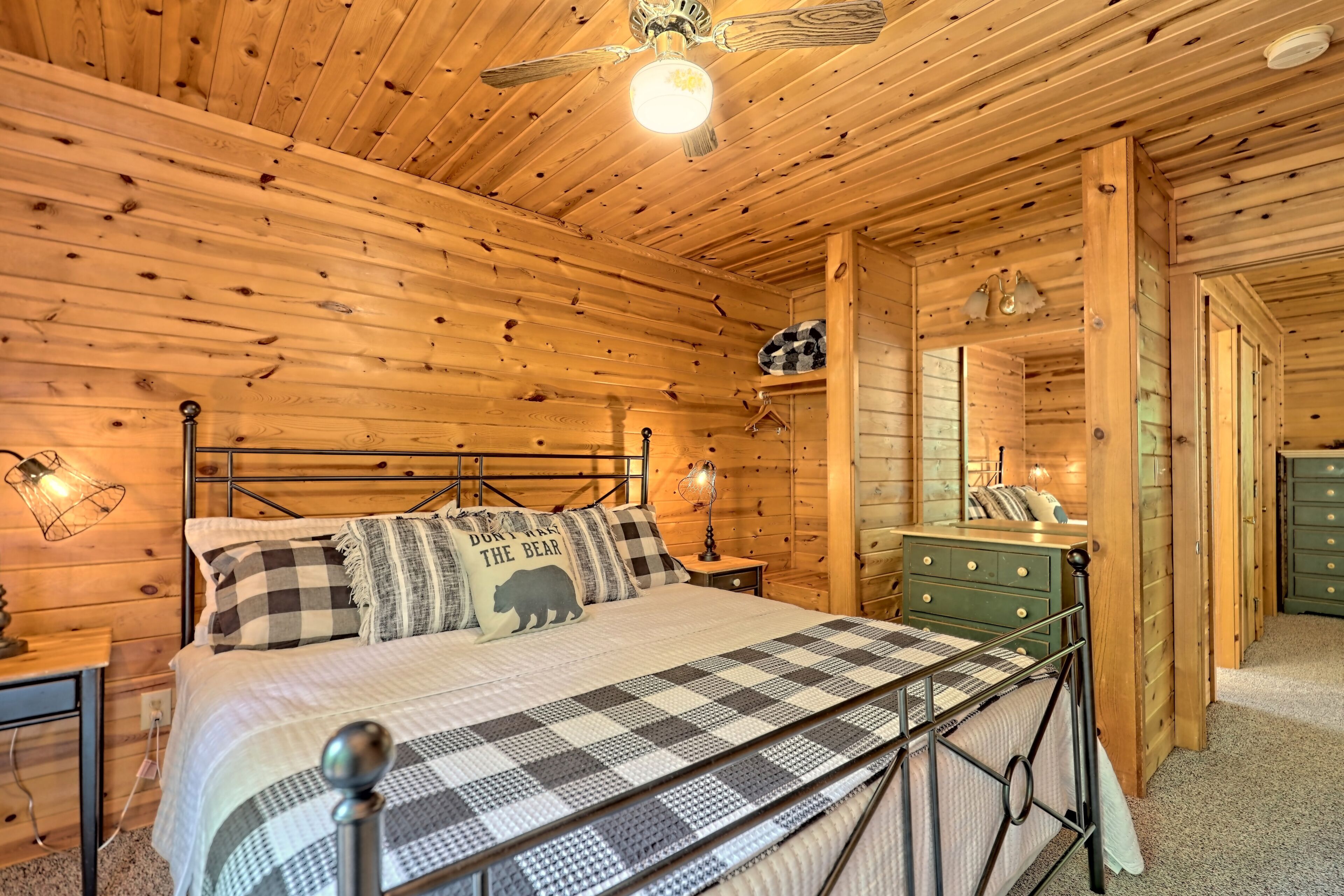 A wooden cabin bedroom with a bed, a dresser, a hanging light fixture, and a ceiling fan.