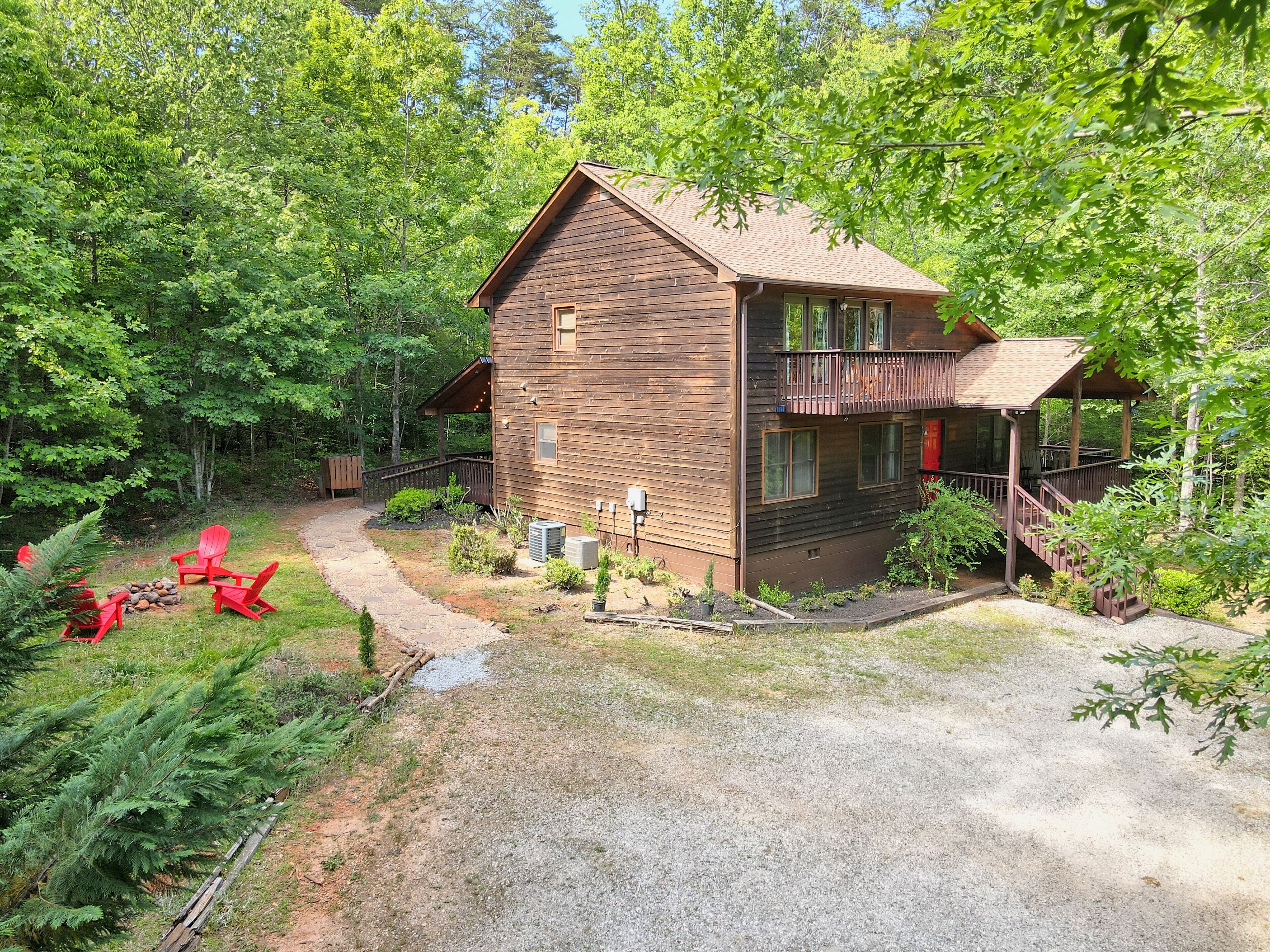 A two-story wooden cabin with a covered porch and a gravel driveway.