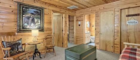 A wooden cabin interior with a rocking chair, a table, a green chest of drawers, a framed wildlife picture, and a sign indicating a private laundry room.