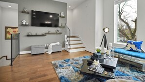 Een moderne woonkamer met een flatscreen televisie, een trap, een blauwe bank en een houten vloer.
