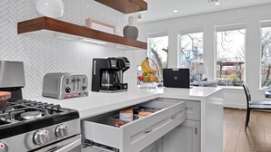 Een moderne keuken met een gasfornuis, een broodrooster, een koffiezetapparaat en een schaal met fruit op het aanrecht.