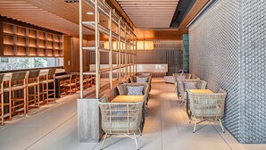 Ein modernes Interieur mit Holzbodenpaneelen, einer zentralen Sitzecke mit Korbstühlen und einer Wand mit Muster.
