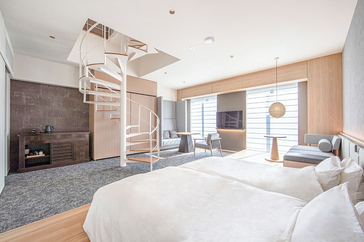 A modern hotel room with a spiral staircase, a large bed, a seating area, and a view of the city.