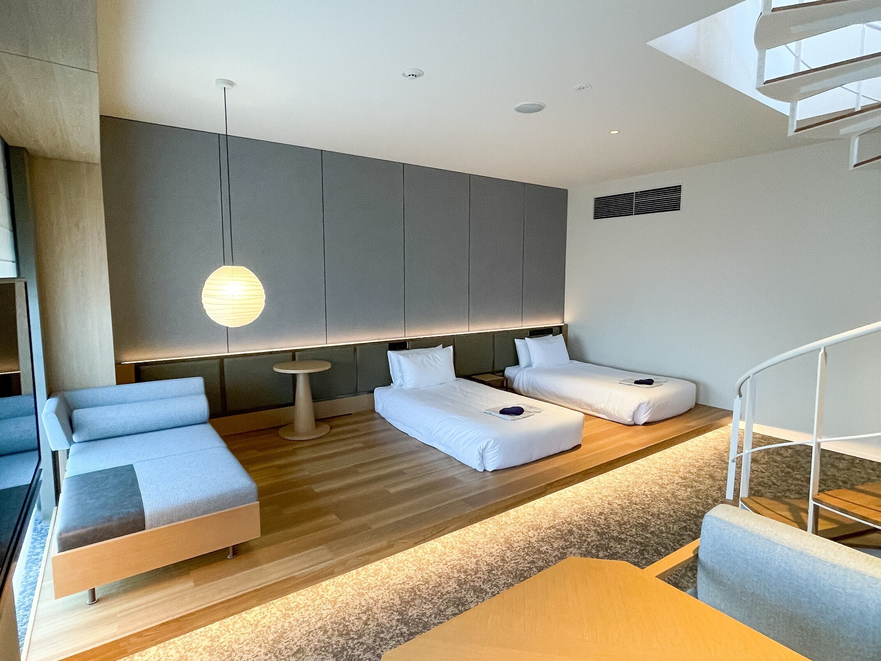 Habitación de hotel moderna con diseño minimalista, que incluye dos camas, un sofá, una mesita y una escalera.