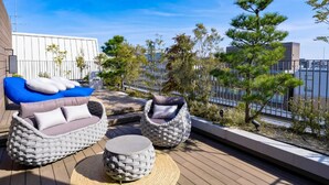 Eine Dachterrasse mit Korbmöbeln, einem blauen Sofa und Blick auf die Stadt.
