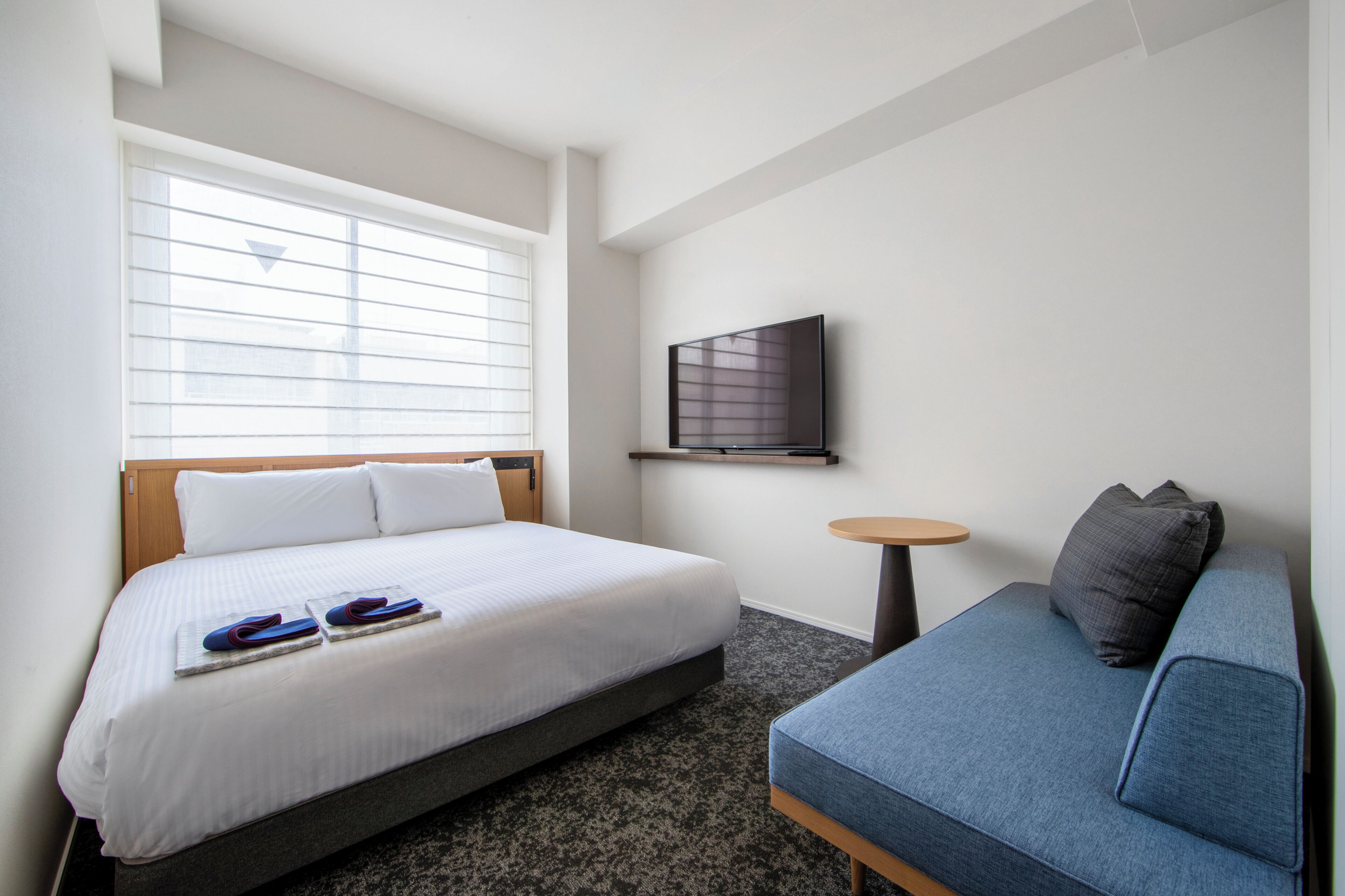 Een hotelkamer met een bed, een sofa, een televisie en een raam met zonwering.