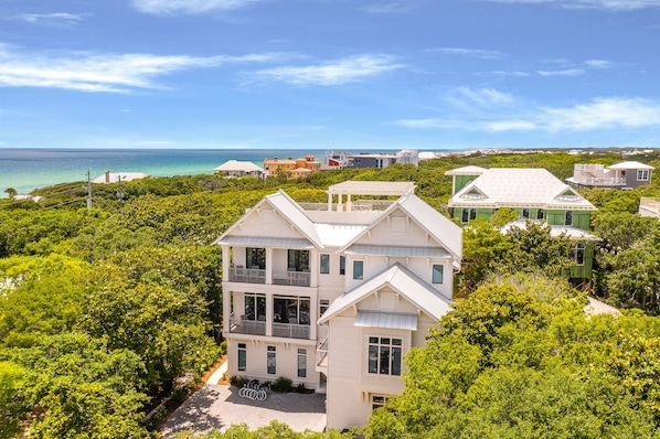 A multi-story house with a balcony, surrounded by lush greenery and a view of the ocean.