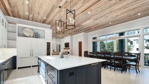 Una cocina moderna con una isla grande, armarios blancos y techo de madera.