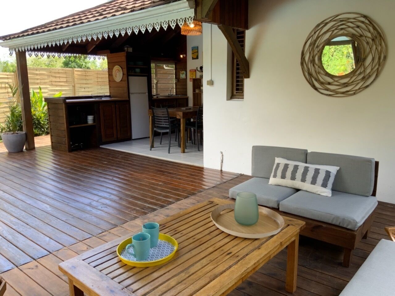 Una terraza de madera con un sofá, una mesa, una pequeña cocina y un ventanal circular.