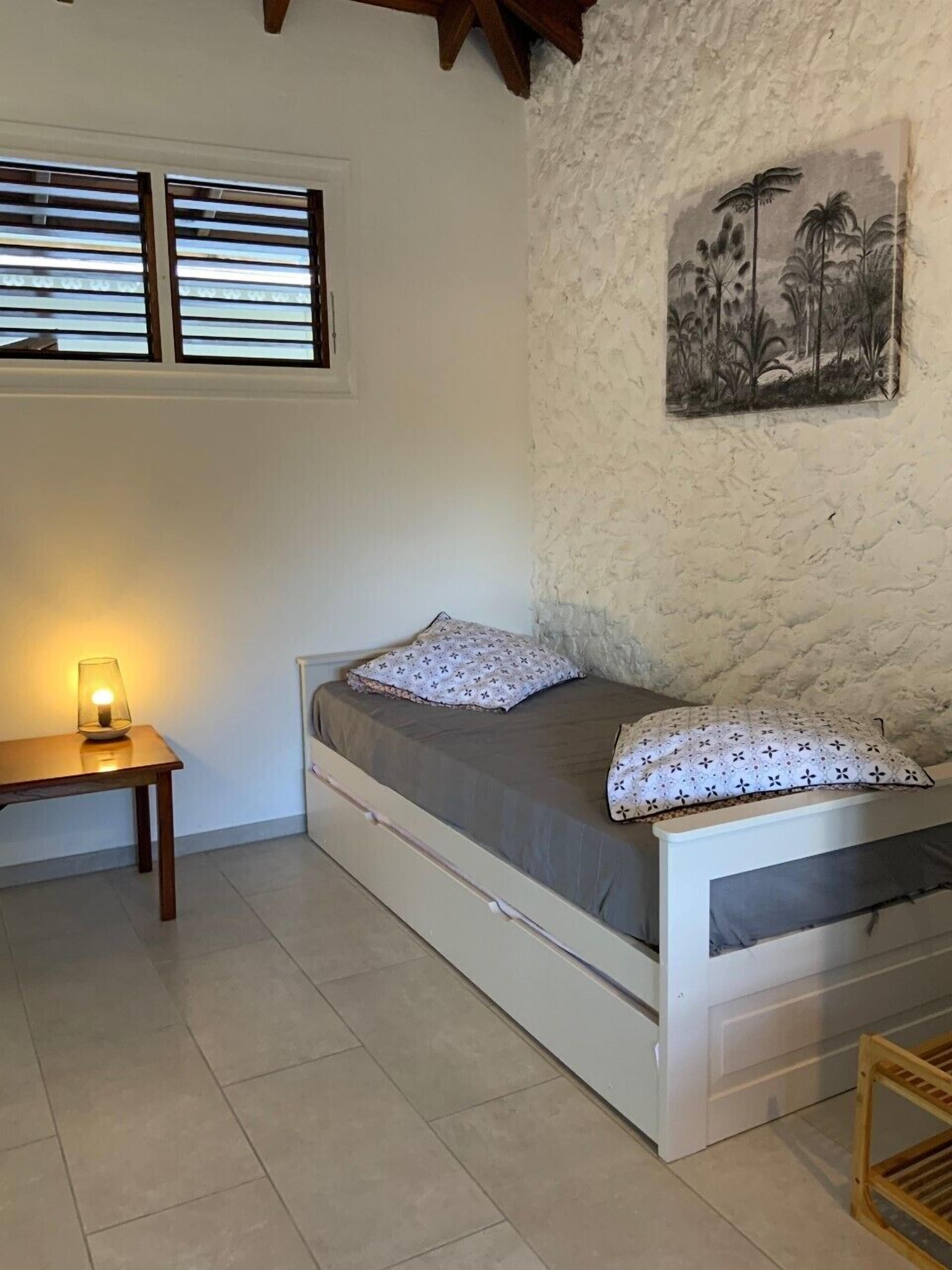 A single bed with a headboard, a bedside table with a lamp, and a wall-mounted painting.