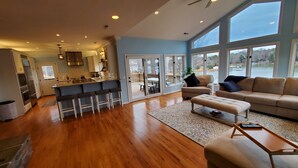 A spacious living area with a large window, a kitchen with a sliding door to the patio, and a cozy seating area with a sofa and ottoman. - Updated Lakefront Home w/new Hot Tub & deep water dock, Sleeps 12. (Mooresville)