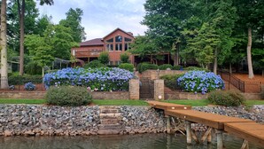 A house with a large front yard, a wooden deck, and a stone wall. - Updated Lakefront Home w/new Hot Tub & deep water dock, Sleeps 12. (Mooresville)