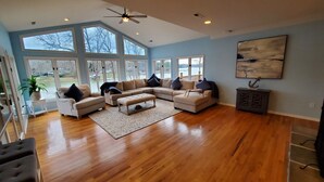A spacious living room with a sectional sofa, a coffee table, and a large window overlooking a lake. - Updated Lakefront Home w/new Hot Tub & deep water dock, Sleeps 12. (Mooresville)