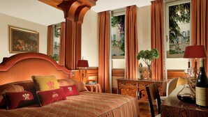 A hotel room with a large bed, a wooden headboard, a desk with a chair, and a view of a building through the window. - Bio Hotel Raphael - Relais Chateaux (Rome)