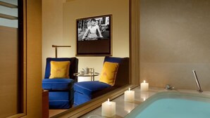 A modern bathroom with a bathtub, two blue chairs with yellow cushions, a small table with a teapot, and a framed black and white photo on the wall. - Bio Hotel Raphael - Relais Chateaux (Rome)