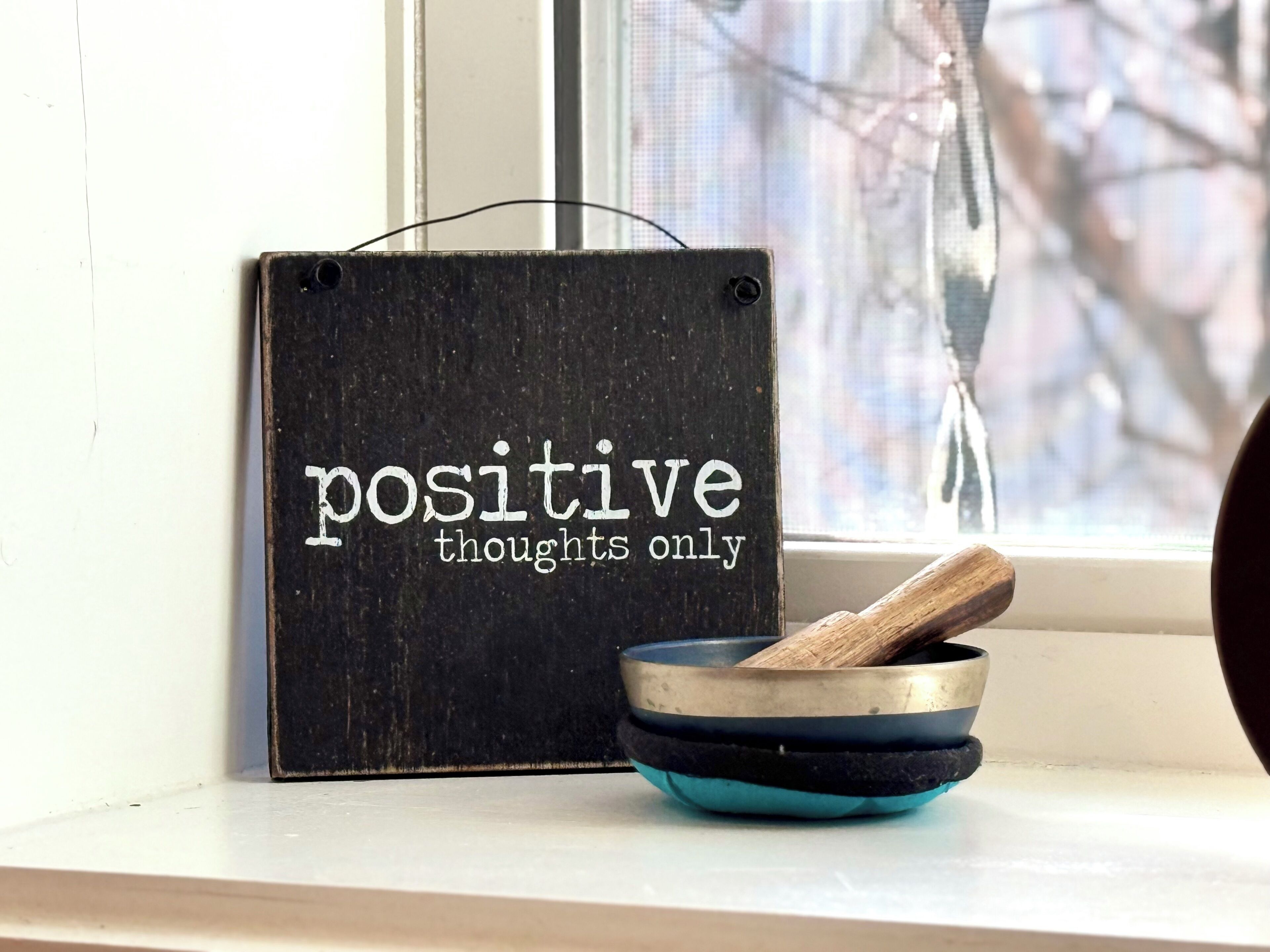 A sign with the words 'positive thoughts only' and a bowl with a spoon on a windowsill.