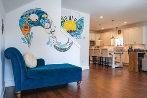 A modern living room with a blue sofa, a kitchen in the background, and a wall mural.