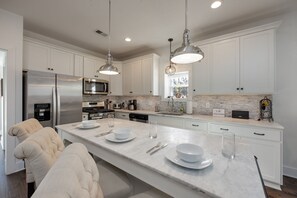 A modern kitchen with white cabinetry, stainless steel appliances, and pendant lighting.