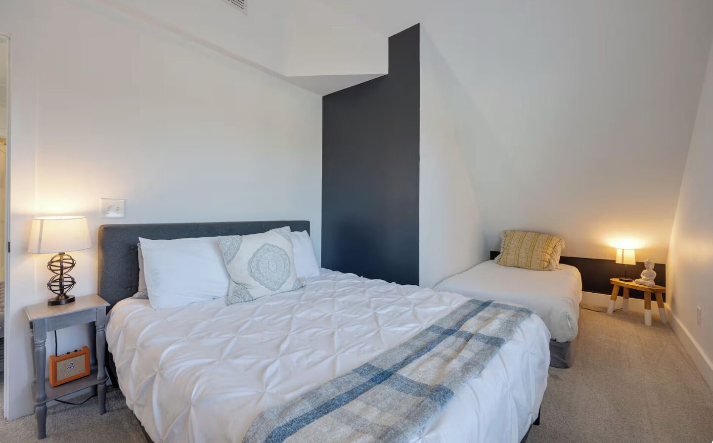 Ein Hotelzimmer mit einem großen Bett, einem kleineren Bett, einem Nachttisch mit Lampe und einem Sessel.