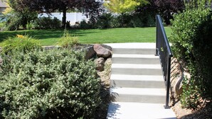 Un escalier en béton avec une rampe métallique menant à une pelouse.