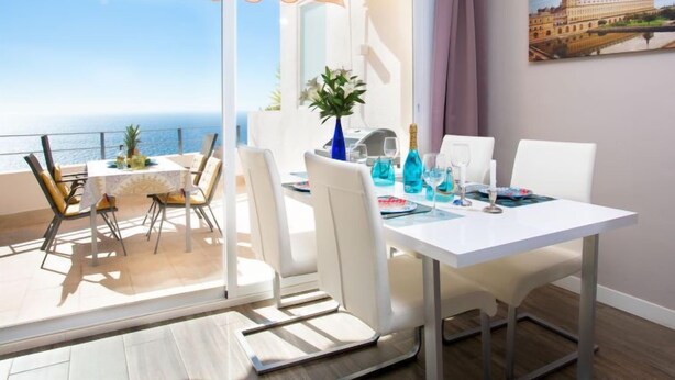 Een balkon met uitzicht op zee, een eettafel met stoelen en een schilderij aan de muur.