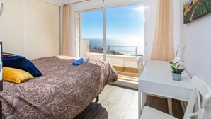 Een slaapkamer met een bed, een bureau en uitzicht op zee.