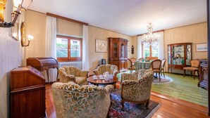A room with patterned armchairs, a wooden cabinet, a dining table with chairs, and a chandelier. - La Verbanina 2 - Lake Maggiore Views Duplex for 4, Ghiffa, Italy (Ghiffa)