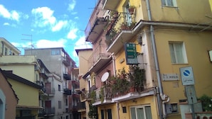 A narrow street with yellow buildings, balconies with plants, and a sign for B&B Casa Giulio. - Large Triple Room for max 3 people (Taormina)