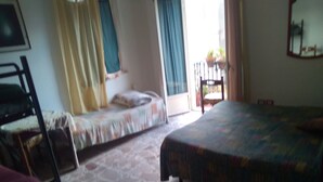 A bedroom with two beds, a chair, a window with curtains, and a view of the outside. - Large Triple Room for max 3 people (Taormina)