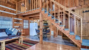Un intérieur de chalet en bois spacieux, avec un escalier central, un coin salon doté d’un canapé et d’une table basse, et un espace cuisine.