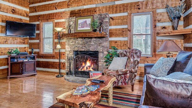 L’intérieur d’une cabane en rondins, avec une cheminée en pierre, des meubles en bois et un téléviseur fixé au mur.