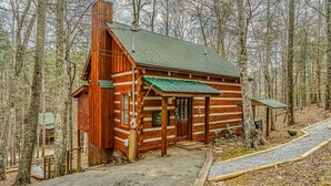 Une cabane en rondins surmontée d’un toit végétalisé, entourée d’une forêt.
