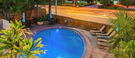 Una piscina con cubierta de madera, rodeada de palmeras y sillas.