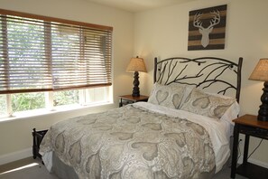 Ein Schlafzimmer mit einem Bett, zwei Nachttischen, einem Fenster mit Jalousien und einem Hirschgeweih als Wandbild.