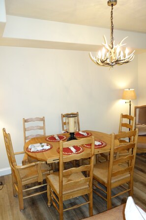 Ein Essbereich mit einem runden Holztisch, sechs Holzstühlen, einer Chandelüster und einer Lampe.
