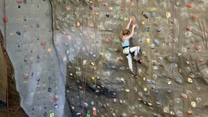 Una pared de escalada con presas de distintos colores y una persona escalando.