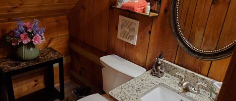 Baño de cabaña de madera con inodoro, lavamanos y una pequeña mesa con un florero.