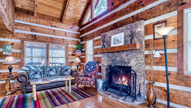 A cozy log cabin interior with a stone fireplace, wooden walls, and a sofa set. - Twin Bear II - Spring and Summer in the Smokies With an EV Charger for Guests! (Sevierville)