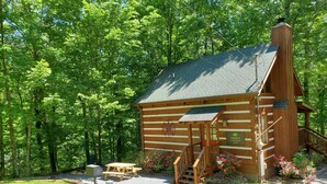 A log cabin with a deck, picnic table, and flower beds. - Twin Bear II - Spring and Summer in the Smokies With an EV Charger for Guests! (Sevierville)