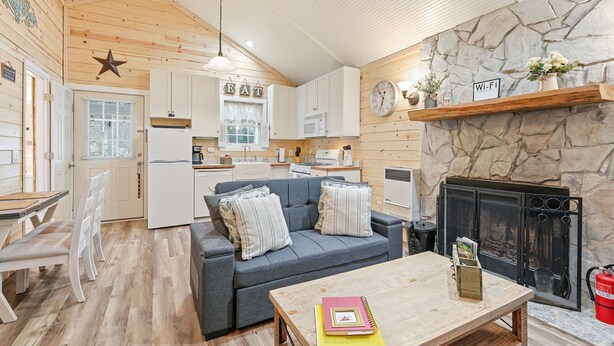 A cozy cabin interior with a dining area, a sofa, a fireplace, and a kitchen. - Riverfront Cottage / Fish Camp Getaway (Newland)