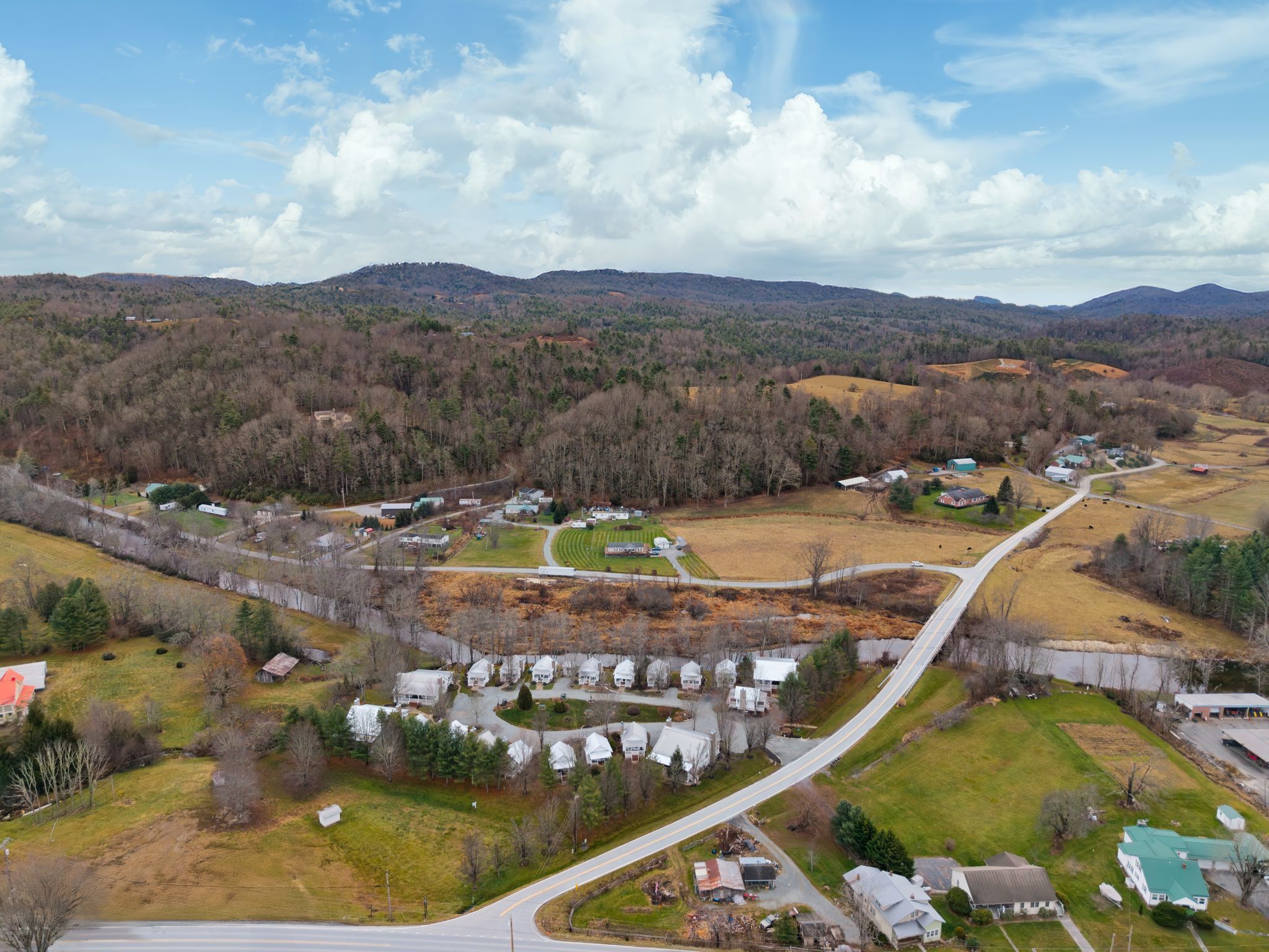 An aerial view of a rural area with a mix of residential houses, a main road, and surrounding fields.