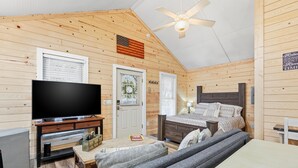 A cozy cabin-style room with a flat-screen TV, a bed, a sofa, and a ceiling fan. - Riverfront Cottage / Fish Camp Getaway (Newland)