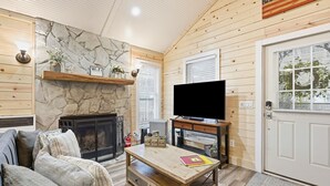 A cozy living room with a stone fireplace, wooden walls, a flat-screen TV, and a comfortable couch. - Riverfront Cottage / Fish Camp Getaway (Newland)