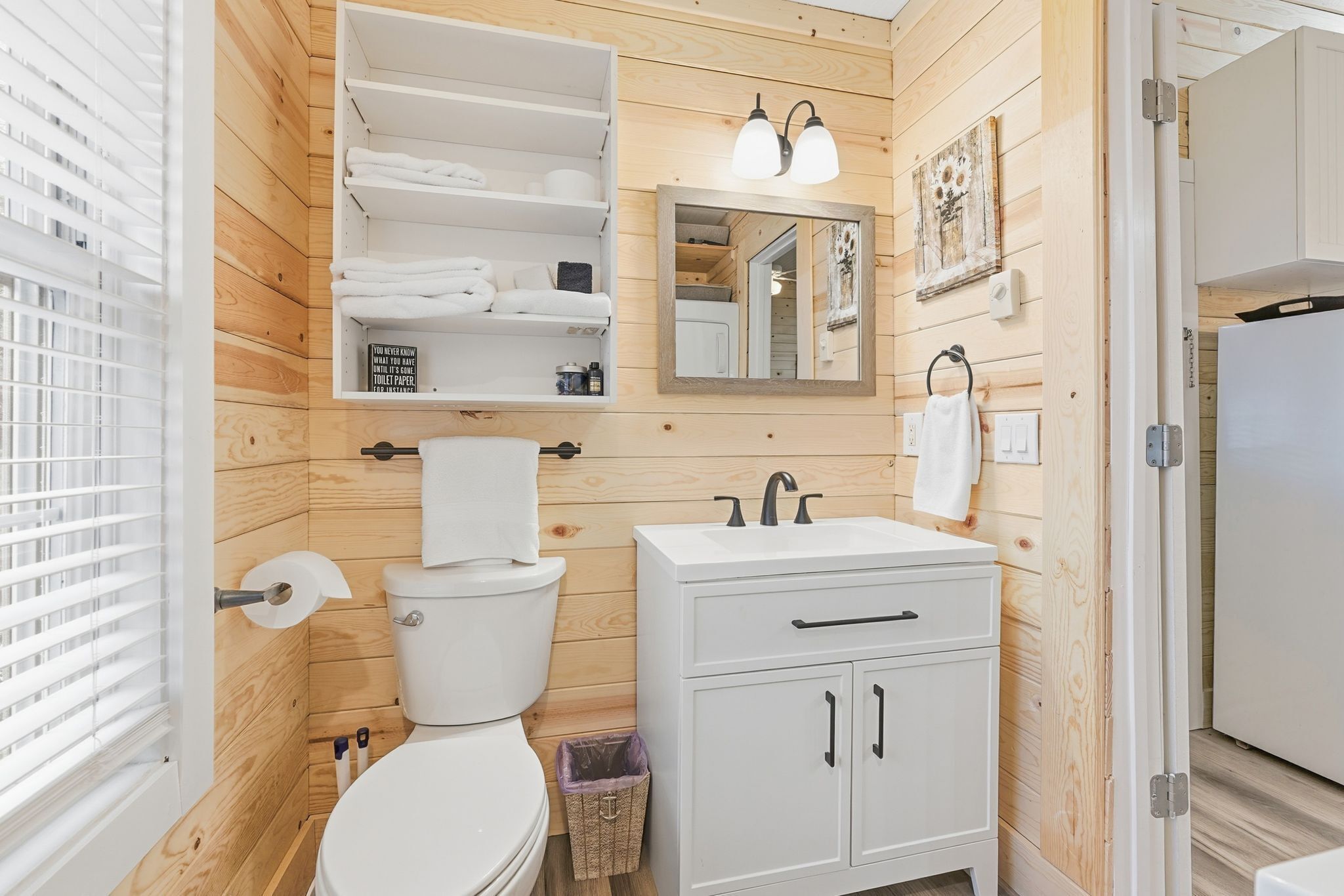 A compact bathroom with wooden paneling, a toilet, a sink with a mirror, and a towel rack.