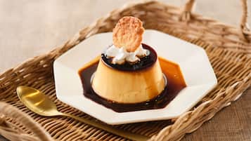 Un dessert servi dans une assiette blanche, accompagné d’une cuillère, le tout posé sur un tapis tissé.