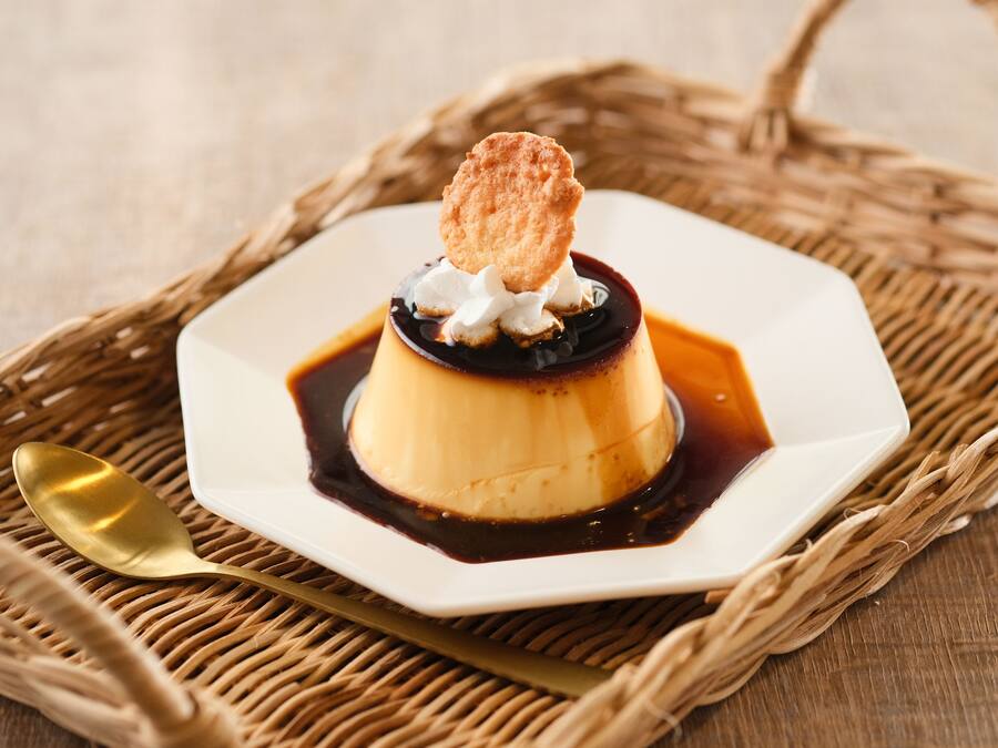 Un dessert servi dans une assiette blanche, accompagné d’une cuillère, le tout posé sur un tapis tissé.