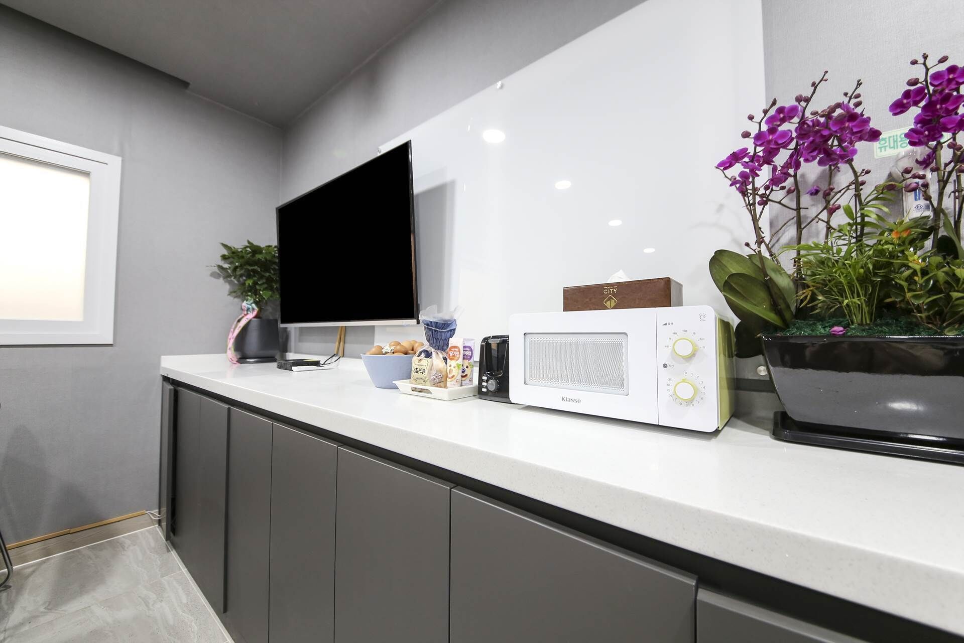 A modern kitchen with a flat-screen TV, a radio, and a potted orchid.